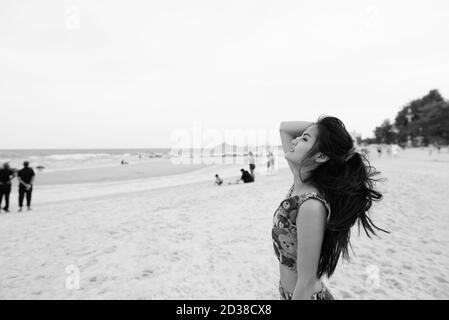 Vista di profilo di giovani felici bella donna asiatica sorridente e guardando verso l'alto la spiaggia pubblica di Hua Hin in Thailandia Foto Stock