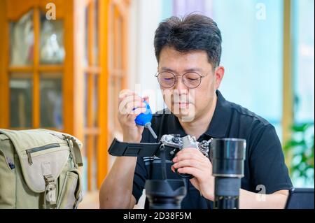 Un uomo asiatico di mezza età il cui hobby è una fotocamera reflex a pellicola da 35mm/135mm. Foto Stock