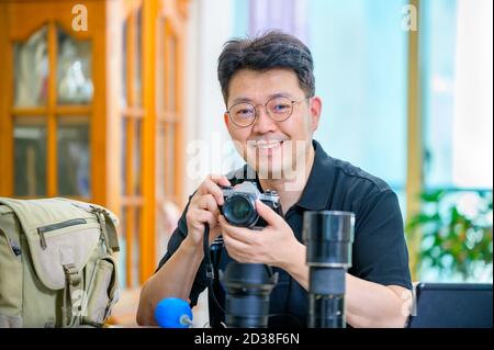 Un uomo asiatico di mezza età il cui hobby è una fotocamera reflex a pellicola da 35mm/135mm. Foto Stock