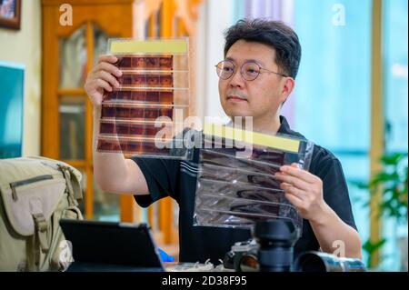 Un uomo asiatico di mezza età il cui hobby è una fotocamera reflex a pellicola da 35mm/135mm. Foto Stock