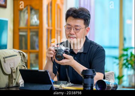 Un uomo asiatico di mezza età il cui hobby è una fotocamera reflex a pellicola da 35mm/135mm. Foto Stock