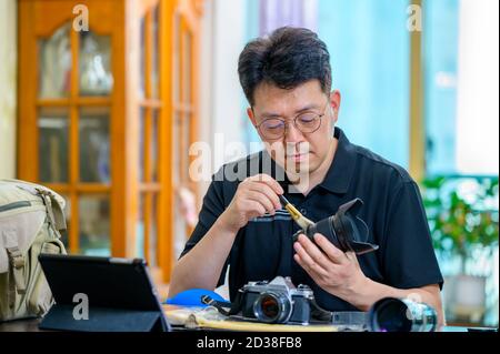 Un uomo asiatico di mezza età il cui hobby è una fotocamera reflex a pellicola da 35mm/135mm. Foto Stock