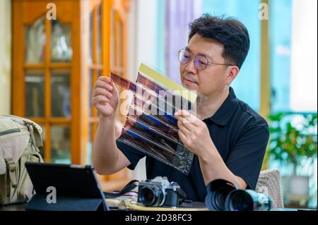 Un uomo asiatico di mezza età il cui hobby è una fotocamera reflex a pellicola da 35mm/135mm. Foto Stock