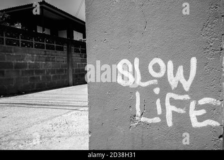 Slow Life segno scritto su muro di cemento contro la vista di vecchio edificio e strada vuota Foto Stock