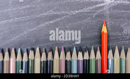 Matite di colore rosso il colore in piedi fuori dalla folla sulla lavagna a fogli mobili e lavagna Foto Stock