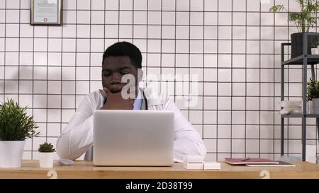 Medico afroamericano che lavora al computer e laptop che legge s Foto Stock