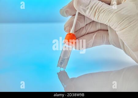 Test del DNA. Provetta con liquido per analisi del DNA e una mano con guanti che tiene un bastone su sfondo blu con riflessione. Foto Stock