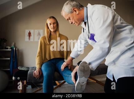 Medico maschile in camice bianco trattando pazienti di sesso femminile feriti ginocchio al centro di riabilitazione Foto Stock