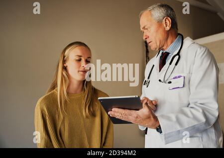 il medico anziano fornisce notizie mediche ai pazienti giovani via a. tablet Foto Stock