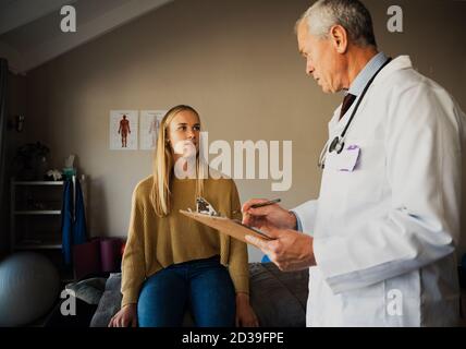Medico maschile anziano che istruisce il consiglio medico a giovane donna malata seduto in ufficio professionale. Foto Stock