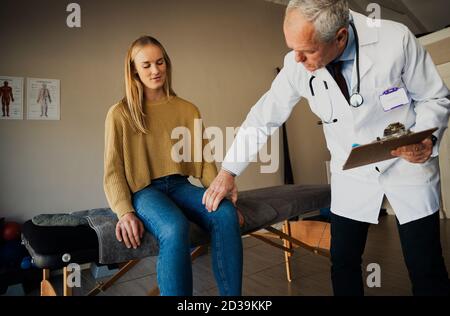 il medico maschile in scrub esamina le giovani pazienti di ginocchio Foto Stock