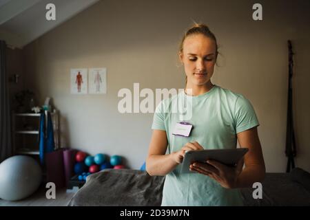 Bella donna caucasica terapeuta su tablet digitale in medicina, centro di riabilitazione Foto Stock