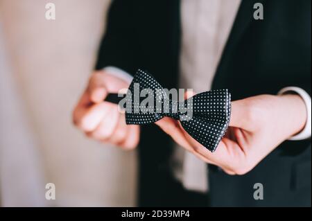 Lo sposo tiene un bowtie nelle sue mani, si vestisce e si prepara per la cerimonia nuziale. Preparazione mattutina degli sposi. Accessori per matrimoni. Persone, busine Foto Stock