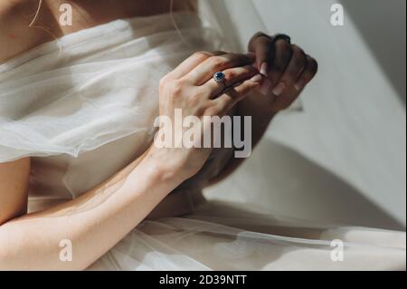 Primo piano di un anello vintage di nozze con un diamante blu sul dito della sposa in un abito da sposa lucido. Mattina della sposa. Il giorno migliore della sposa. Noi Foto Stock