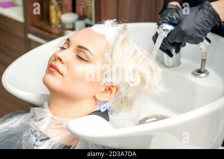 Parrucchiere preparatevi a lavare via la tintura bianca dai capelli di giovane donna caucasica in lavello al salone di bellezza Foto Stock