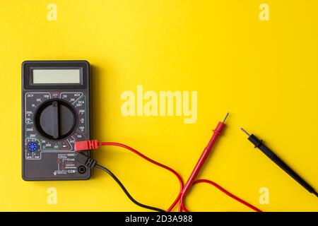 Multimetro digitale con sonde e display retroilluminato su sfondo giallo. Un multimetro o un multitester è uno strumento elettronico di misurazione Foto Stock