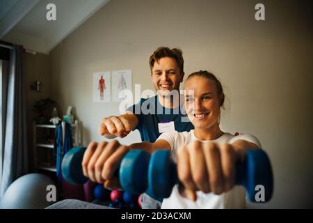 Fisioterapista maschile che istruisce paziente caucasico femmina forma corretta di esercizio con manubri Foto Stock