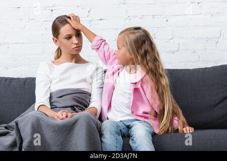 Ragazza che tocca fronte di donna malata avvolta in coperta sopra lettino Foto Stock