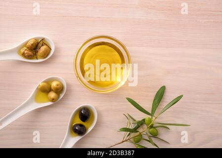 Olio di oliva vegetale in ciotole di vetro su panca da cucina con cucchiaio di olive. Vista dall'alto. Foto Stock