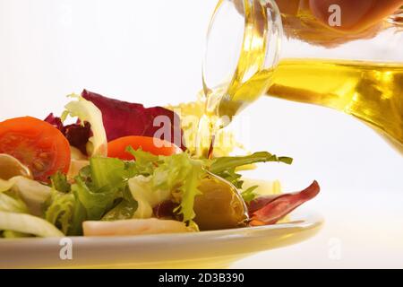 Versare l'olio d'oliva dal distributore dell'olio sull'insalata preparata piastra bianca e sfondo isolato Foto Stock