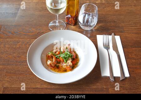 Argenteria su tavolo di legno marrone con piatto rotondo bianco e gamberetti all'aglio. Foto Stock