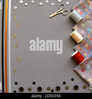 Una plissetta ad occhio di uccello di accessori da cucire con cotone, materiale, forbici, nastri e bottoni su sfondo grigio. Foto Stock
