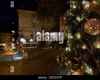 Albero di Natale in primo piano, con decorazioni e luci, sullo sfondo edifici storici di una città italiana su un lago magico e suggestivo Foto Stock