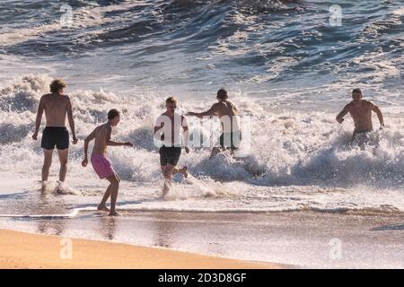 Uomini in vacanza in una vacanza di staycation che corre in mare a Fistral Beach a Newquay in Cornovaglia. Foto Stock