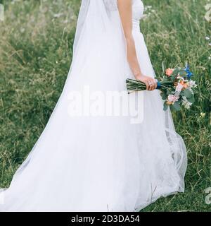 Bel bouquet di nozze nelle mani della sposa in un abito da sposa. Accessori e dettagli per matrimoni. Arrangiamento floreale. Nessuna faccia visibile. Foto Stock