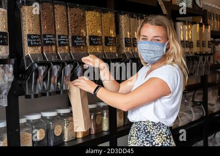 Donna che indossa la maschera viso shopping riempire una borsa di carta con ingredienti sciolti Foto Stock