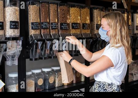 Donna che indossa la maschera viso shopping riempire una borsa di carta con ingredienti sciolti Foto Stock