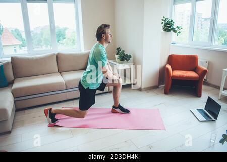 L'uomo biondo caucasico nello sport sta usando un laptop a. a casa mentre si hanno lezioni di fitness digitale Foto Stock