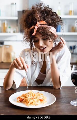 donna riccia che tiene la forcella vicino al piatto con gli spaghetti preparati Foto Stock