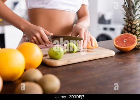 Vista ritagliata di giovane donna che taglia il kiwi vicino a frutta fresca sul tavolo Foto Stock