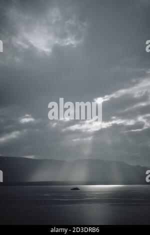 Una nave da crociera soluna in un fiordo e cielo drammatici paesaggio con alberi di luce solare che brillano attraverso le nuvole Dell'Islanda settentrionale Foto Stock