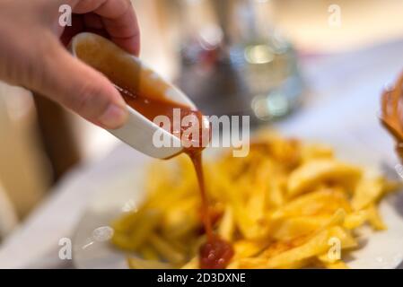 Salsa di pomodoro rosso brillante servita in una piccola ciotola cinese bianca durante una sessione di pranzo, che copre un contorno di patatine salate. Foto Stock