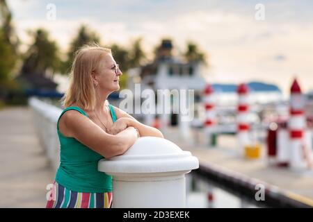 Donna anziana che guarda yacht e barca nel porto. Sport nautici per la famiglia. Lady Walking in resort tropicale in vacanza estiva. Vacanza al mare. Foto Stock