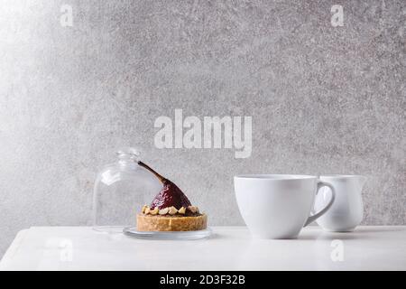 Vino rosso dolce pera tartlet con tazza di caffè espresso e la brocca di crema piedi su marmo bianco tavola con muro grigio a sfondo. Stile minimalista Foto Stock