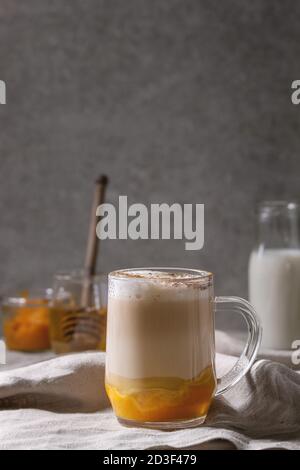 Di vetro stratificato di zucca spice latte con purea di zucca, schiuma di latte e cannella in piedi con gli ingredienti in vasi decorativi e zucche bianco sulla cru Foto Stock