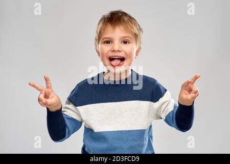 piccolo ragazzo in pullover a righe che mostra la pace Foto Stock