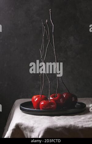 Red caramello mele dolce autunno o di Natale dessert servito con filiali in nero piastra in ceramica su lino tovaglia con muro grigio a sfondo. Da Foto Stock