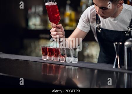 il barista riempie i colpi con il liquore rosso da una bottiglia sul bar. Foto Stock