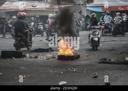 Makassar, Sulawesi del Sud, Indonesia. 8 Ott 2020. I motociclisti che passano sulla strada intorno a pneumatici usati bruciati dagli studenti Makassar mentre protestano contro la ratifica della legge Omnibus. Le manifestazioni contro questa legge continuarono a portarsi per le strade e a bloccare le strade della città. Credit: Herwin Bahar/ZUMA Wire/Alamy Live News Foto Stock