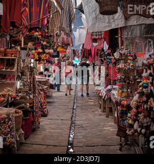 I turisti passeggiano attraverso il mercato di Pisaq, Pisac, Perù, circondato da souvenir e abbigliamento sulle bancarelle del mercato Foto Stock