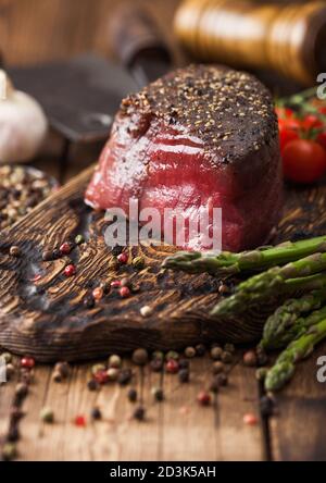 Fetta di manzo crudo fesa giunto con il sale e il pepe sul tagliere di legno con pomodori aglio e punte di asparagi su legno tavolo da cucina. Foto Stock