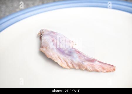 Punta dell'ala di pollo crudo su un piatto. Ossa di pollame rosa di grado umano. Concetto per alimentare la dieta di alimento crudo, modello di preda cruda (PMR) o BARF per i gatti, i cani e l'pe Foto Stock