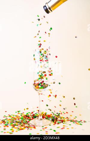 I confetti di Natale si sono riversati con una bottiglia di champagne su un flauto bicchiere di champagne, un'idea creativa per natale, tema natalizio Foto Stock