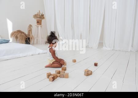 Little bella ragazza afroamericana giocare case con ecmattoni di legno, costruire e distruggere torri. Fine sviluppo motori, giochi educativi. Bianco Foto Stock