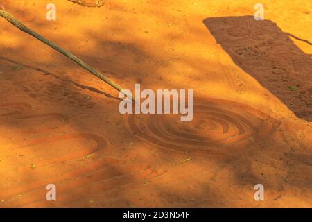 Kings Creek Station, Northern Territory, Australia - 21 agosto 2019: Persone aborigene che creano forme con sabbia rossa sul terreno in arte aborigena Foto Stock