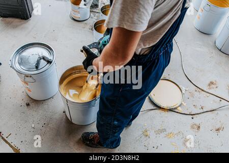 Lavoratore che mescola resina epossidica gialla con il miscelatore in una secchio di stagno Foto Stock